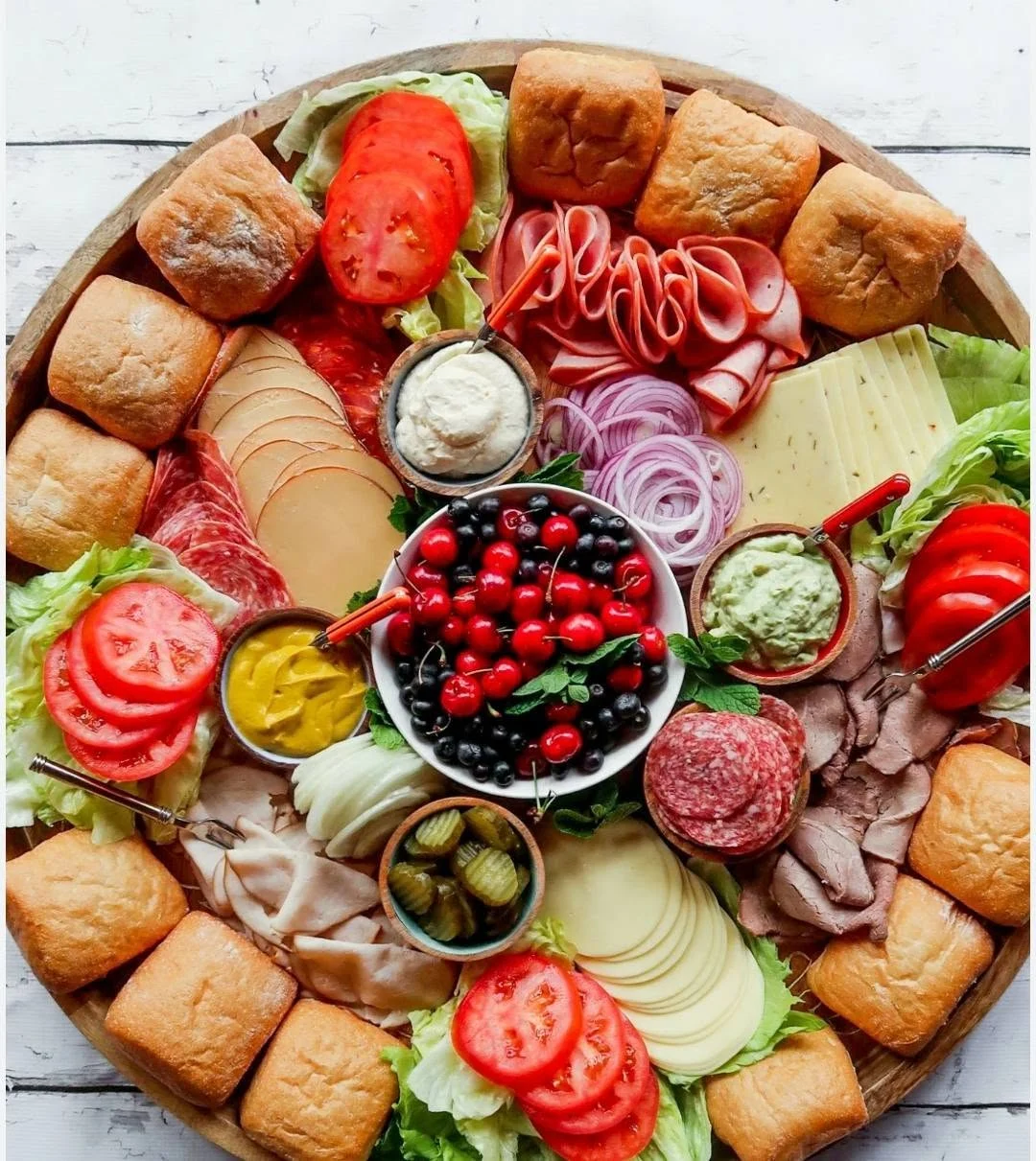 Round build-your-own sandwich board with rolls, deli meats, cheeses, tomatoes and spreads