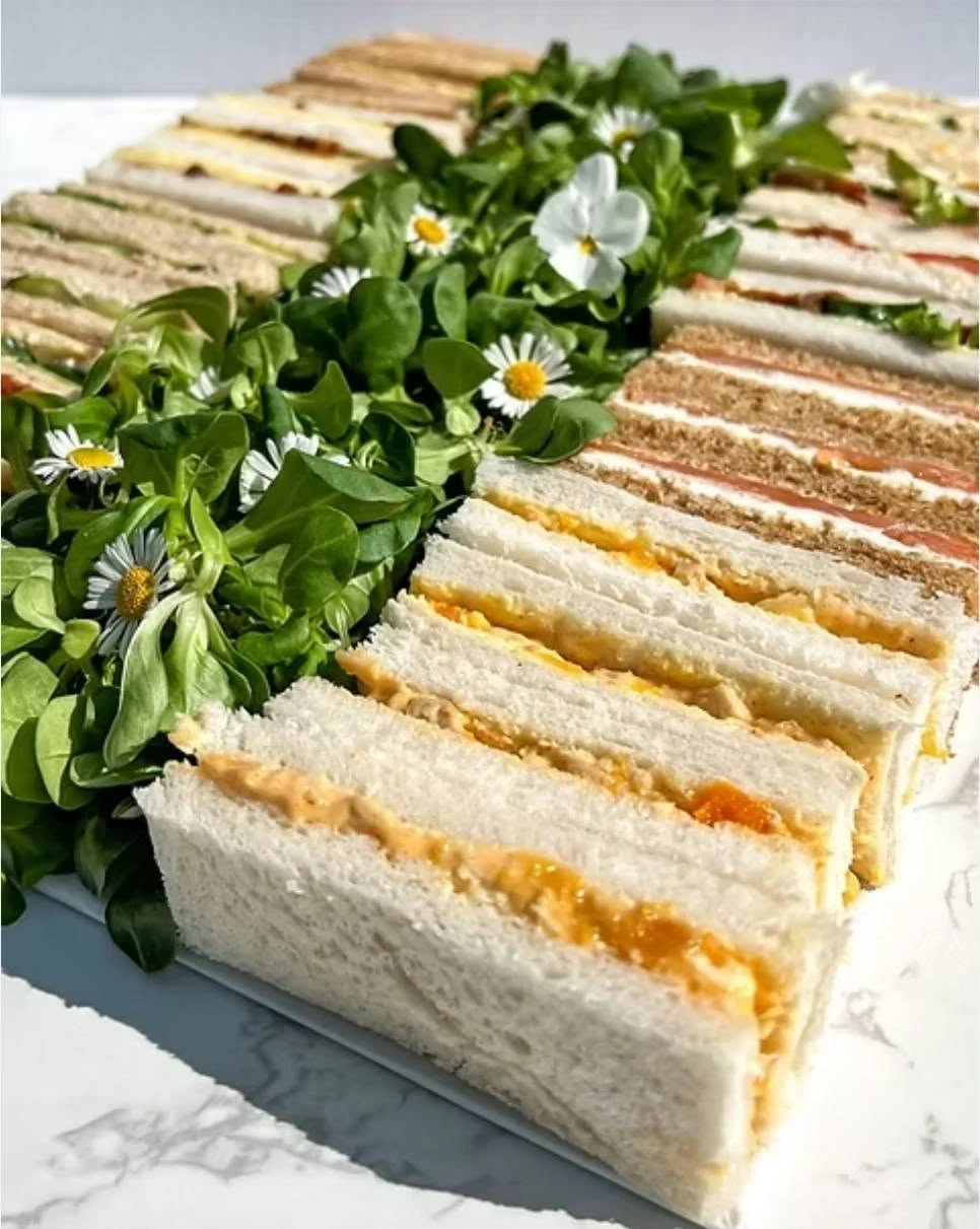 Platter of finger sandwiches with greens and daisies